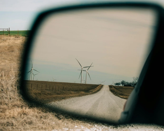 a car's rear view mirror reflecting a wind farm